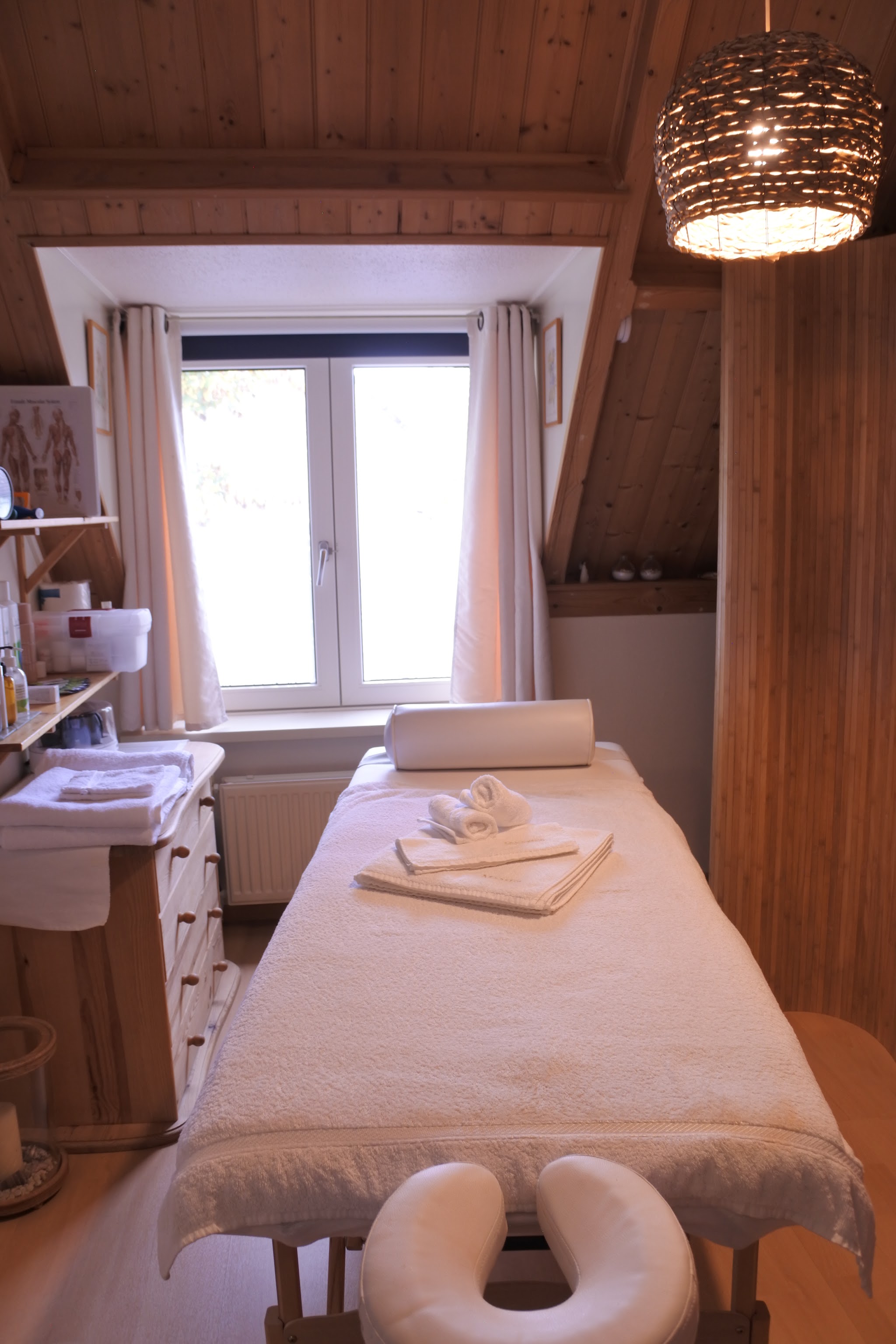 De behandelkamer met massagetafel, opgevouwen handdoeken en houten schuine wand