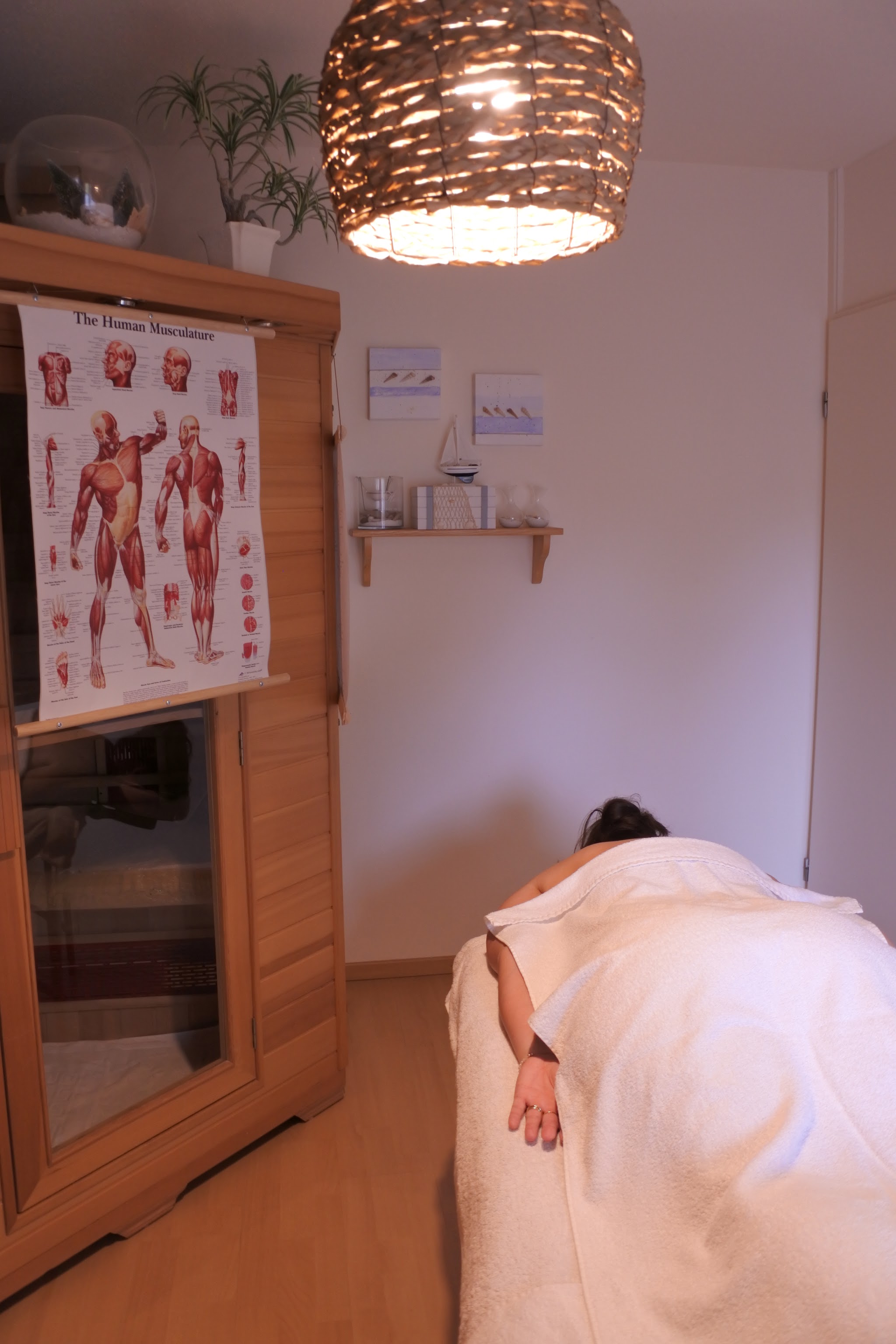De behandelkamer met infraroodcabine en een anatomische spierenkaart aan de wand